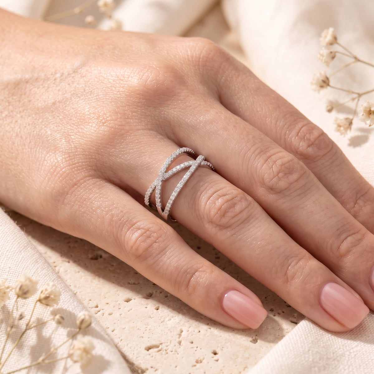 Silver crossover ring with multiple bands and clear pave stones worn on a hand.