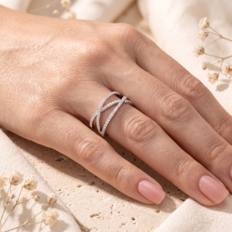 Silver crossover ring with multiple bands and clear pave stones worn on a hand.