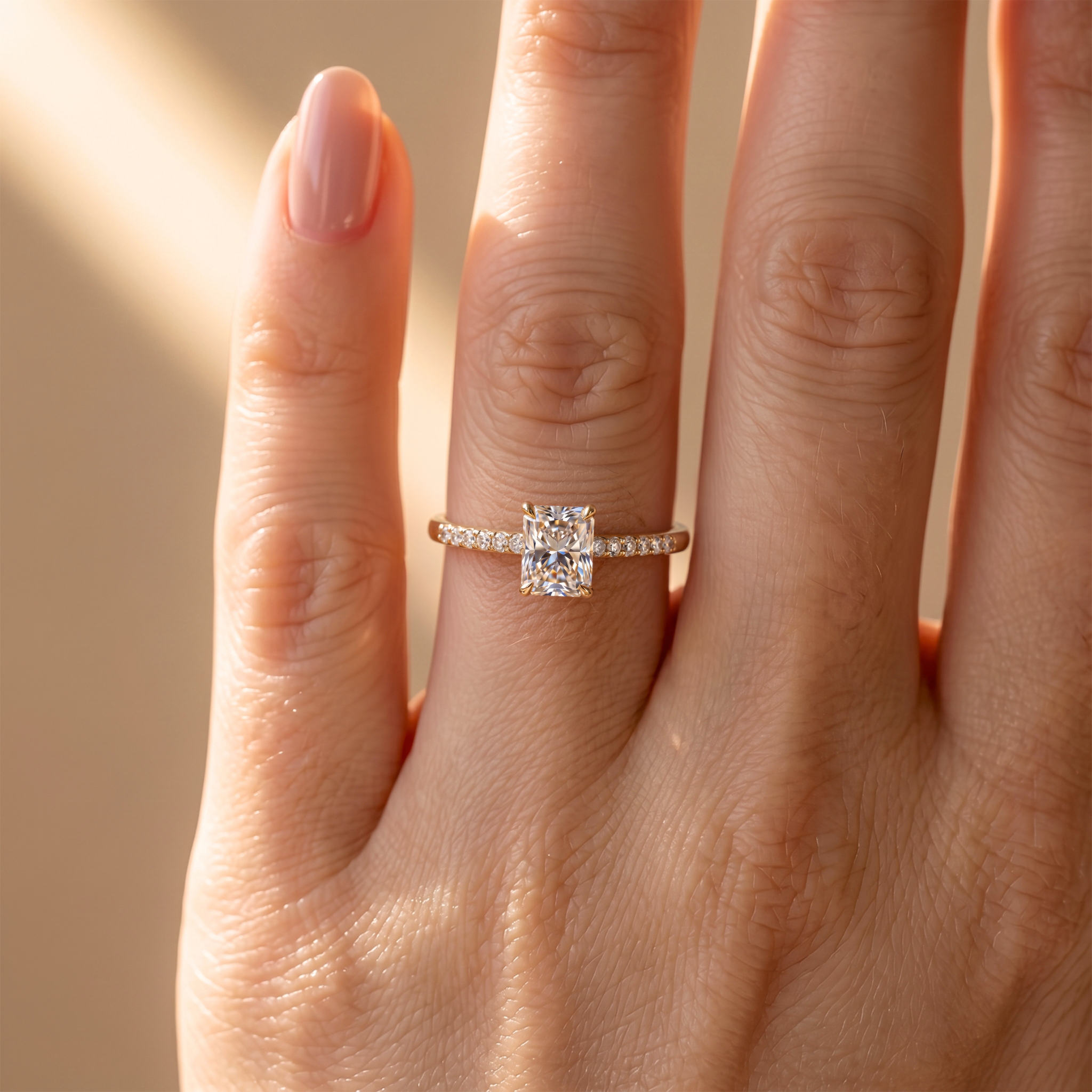 Close-up view of a radiant cut moissanite engagement ring in yellow gold worn on a finger.