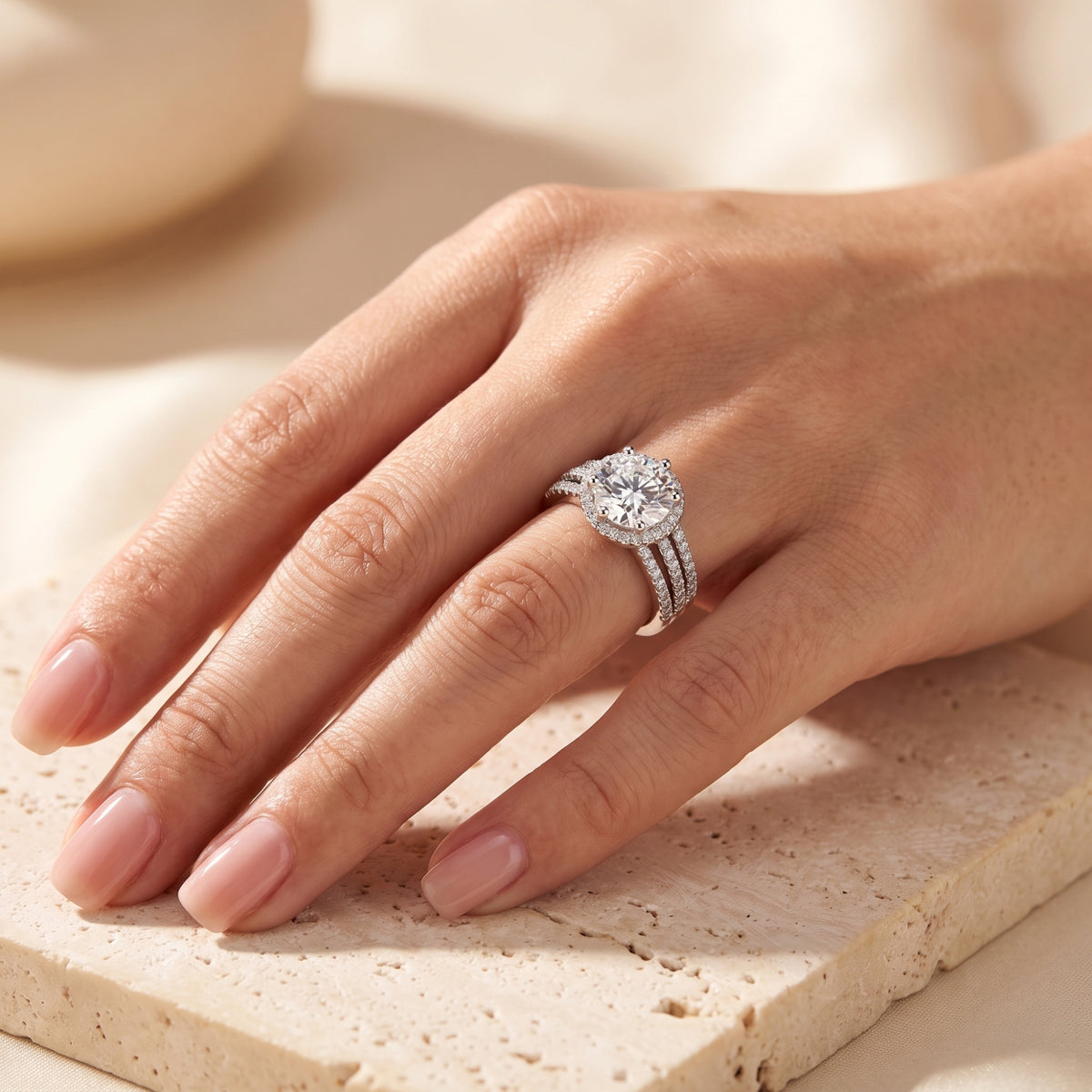 Wider view of the silver triple-band halo ring worn on a finger, with the hand resting on a stone slab.