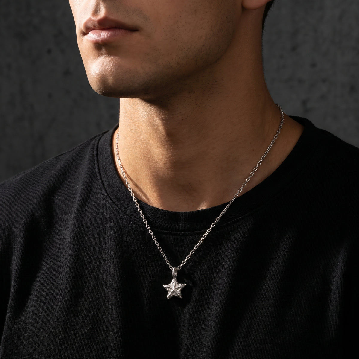 Man wearing the textured silver starburst pendant necklace on a shorter chain over a black T-shirt.