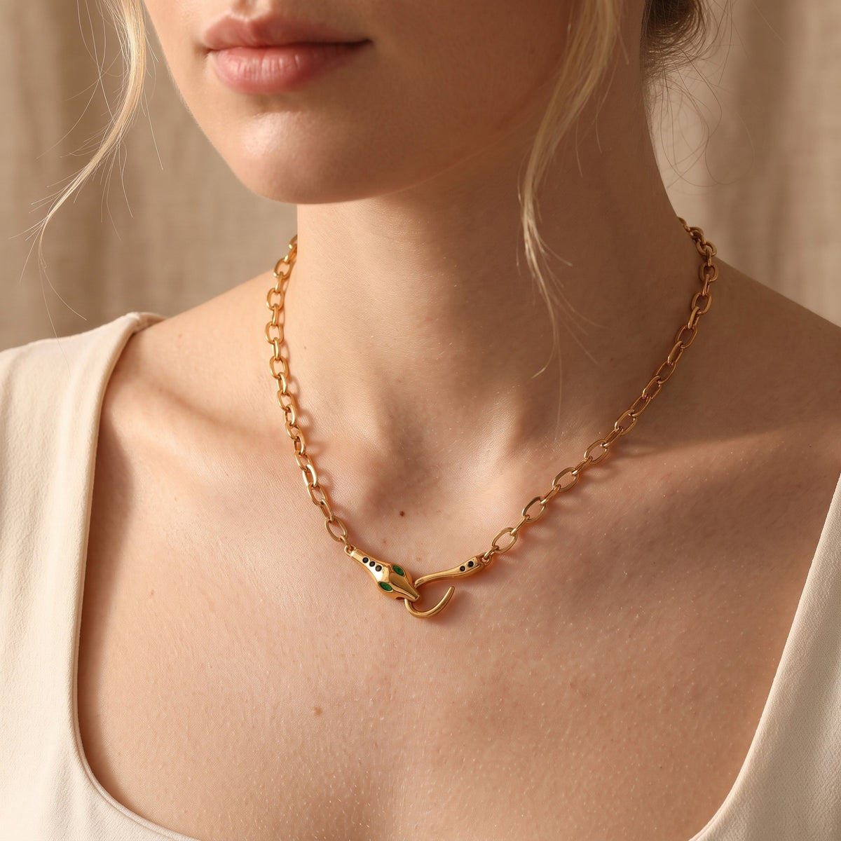 Gold finish stainless steel Serpentine Necklace with a sculptural snake head clasp worn on a woman's neck.