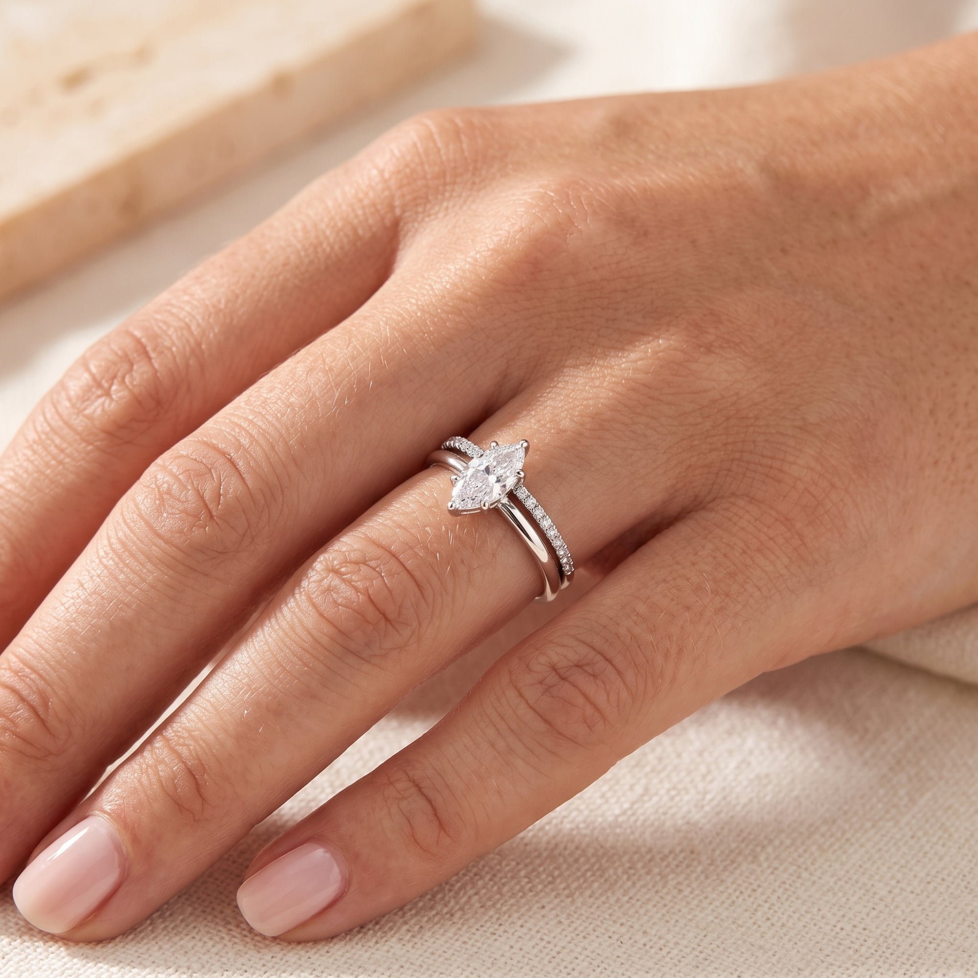 Silver marquise simulated diamond promise ring set worn on a woman's finger against a soft fabric background.