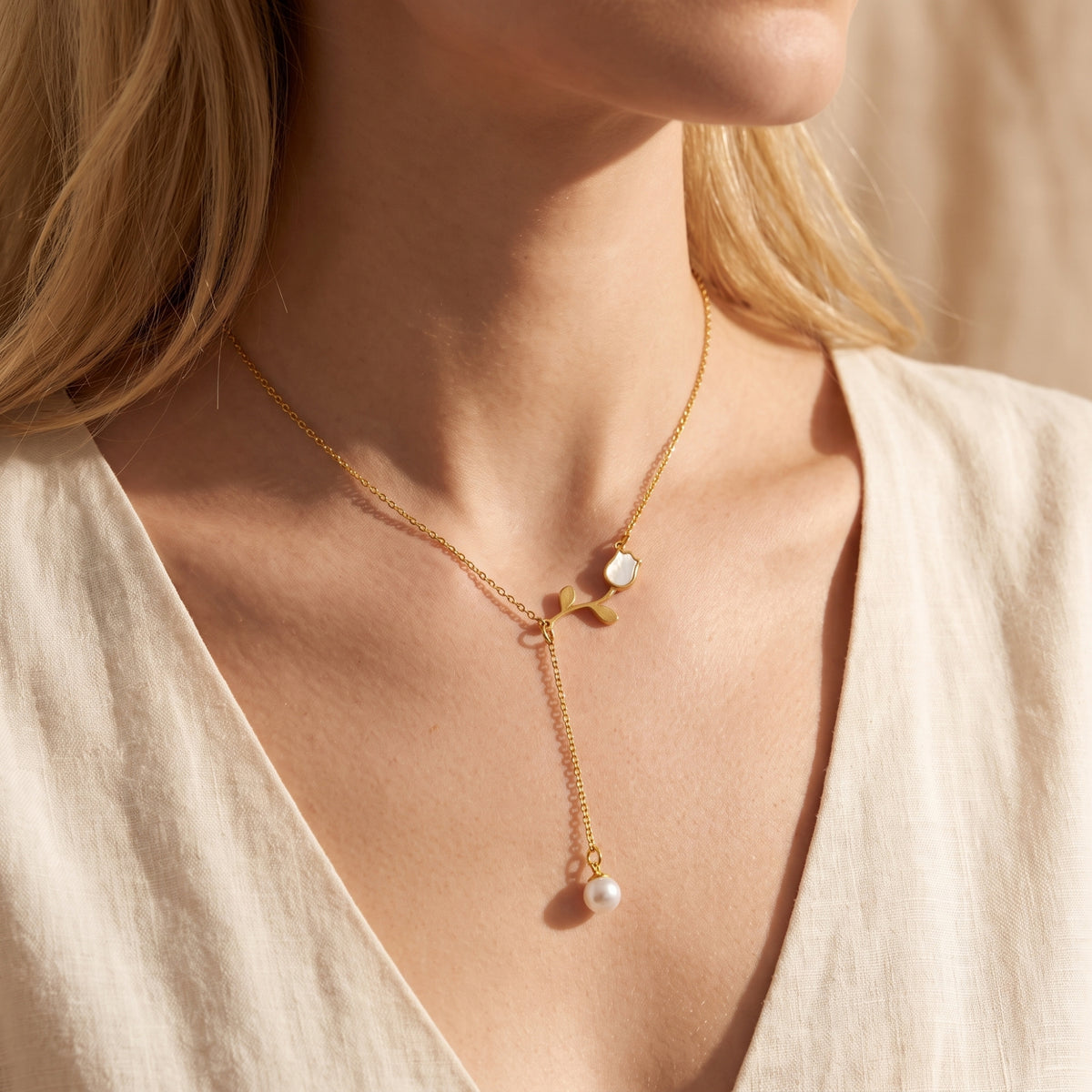 Close-up of a model wearing the gold tulip lariat necklace with a pearl drop over a white V-neck top.