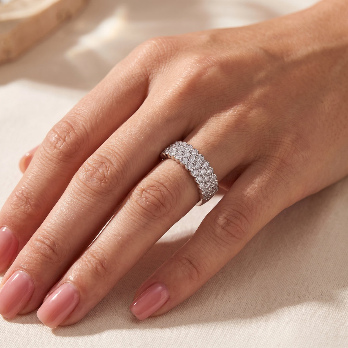 Close angled view of a hand wearing the silver scalloped triple-row clear-stone ring on the ring finger.