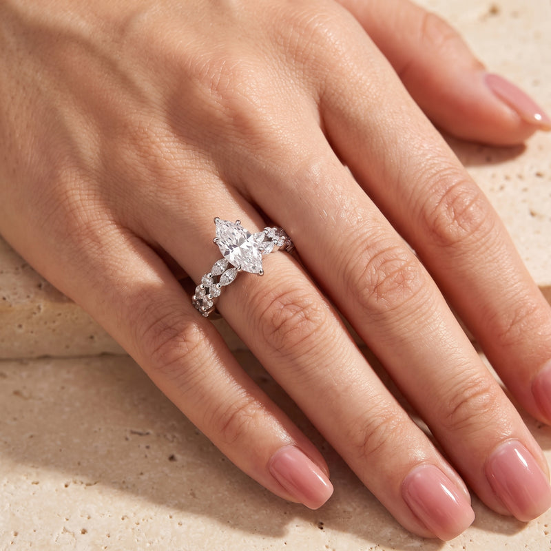 Silver marquise-cut ring set worn on a hand with pale pink polished nails on a textured stone surface.