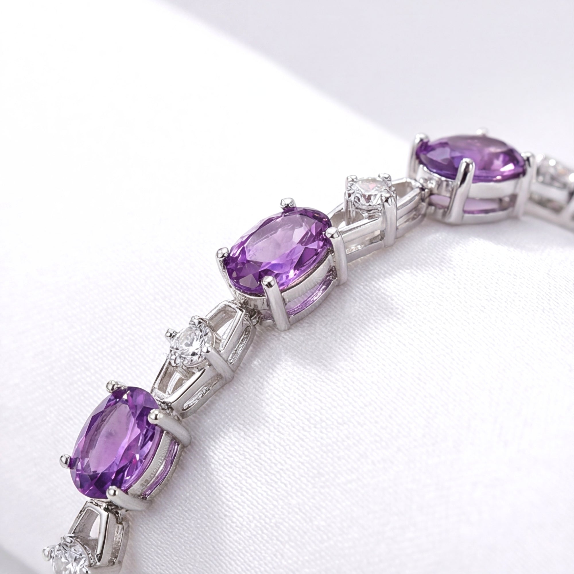 Close-up of oval-cut simulated amethyst and round white stones in a rhodium-finished sterling silver link bracelet.