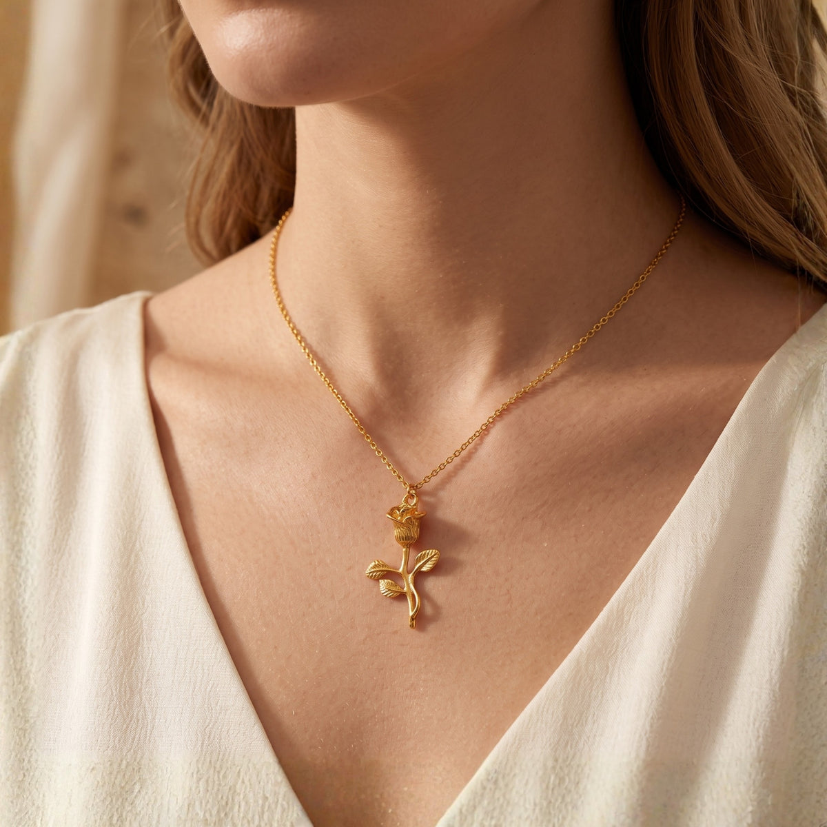 Model wearing a gold-tone rose stem pendant necklace with a white V-neck top.