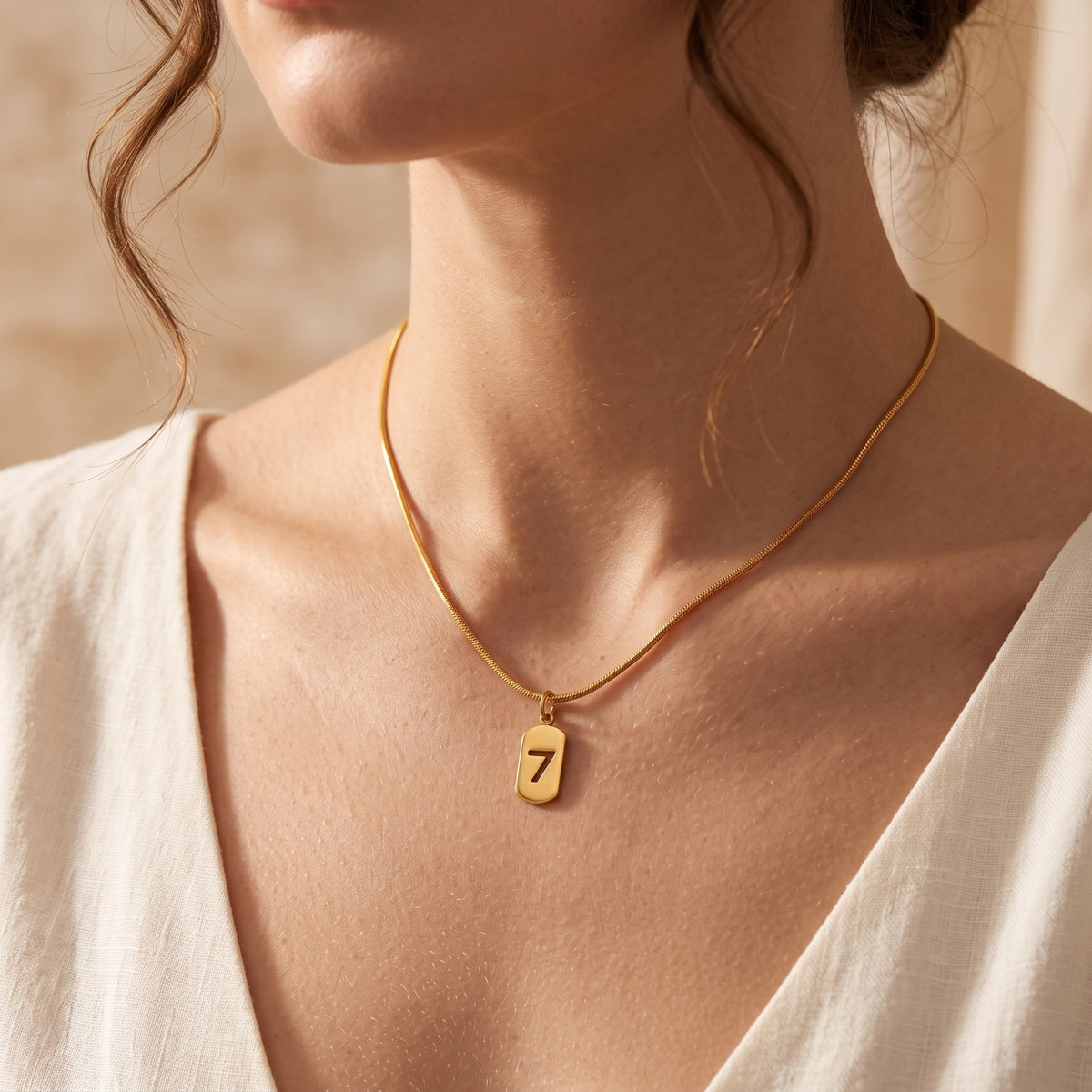 Model wearing the gold-tone cutout number 7 pendant necklace on a snake chain with a V-neck white top.