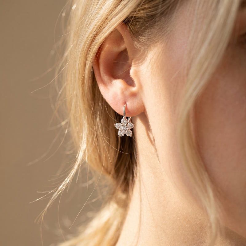 Silver floral drop earring with round moissanite stones worn on ear.