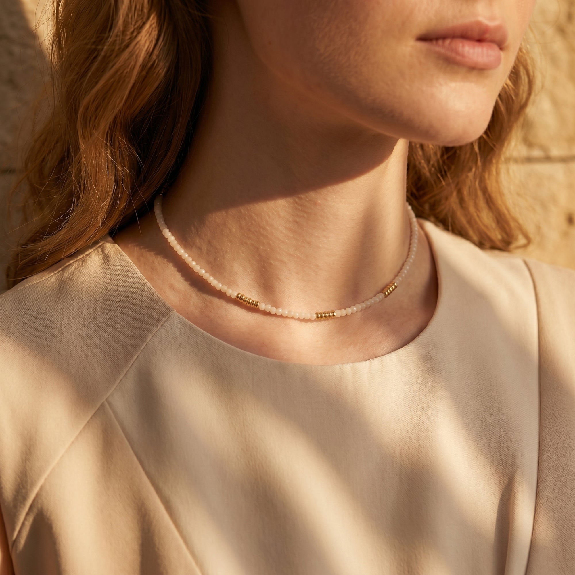 Gold-tone and white quartz beaded necklace worn on a woman's neck in soft natural light.