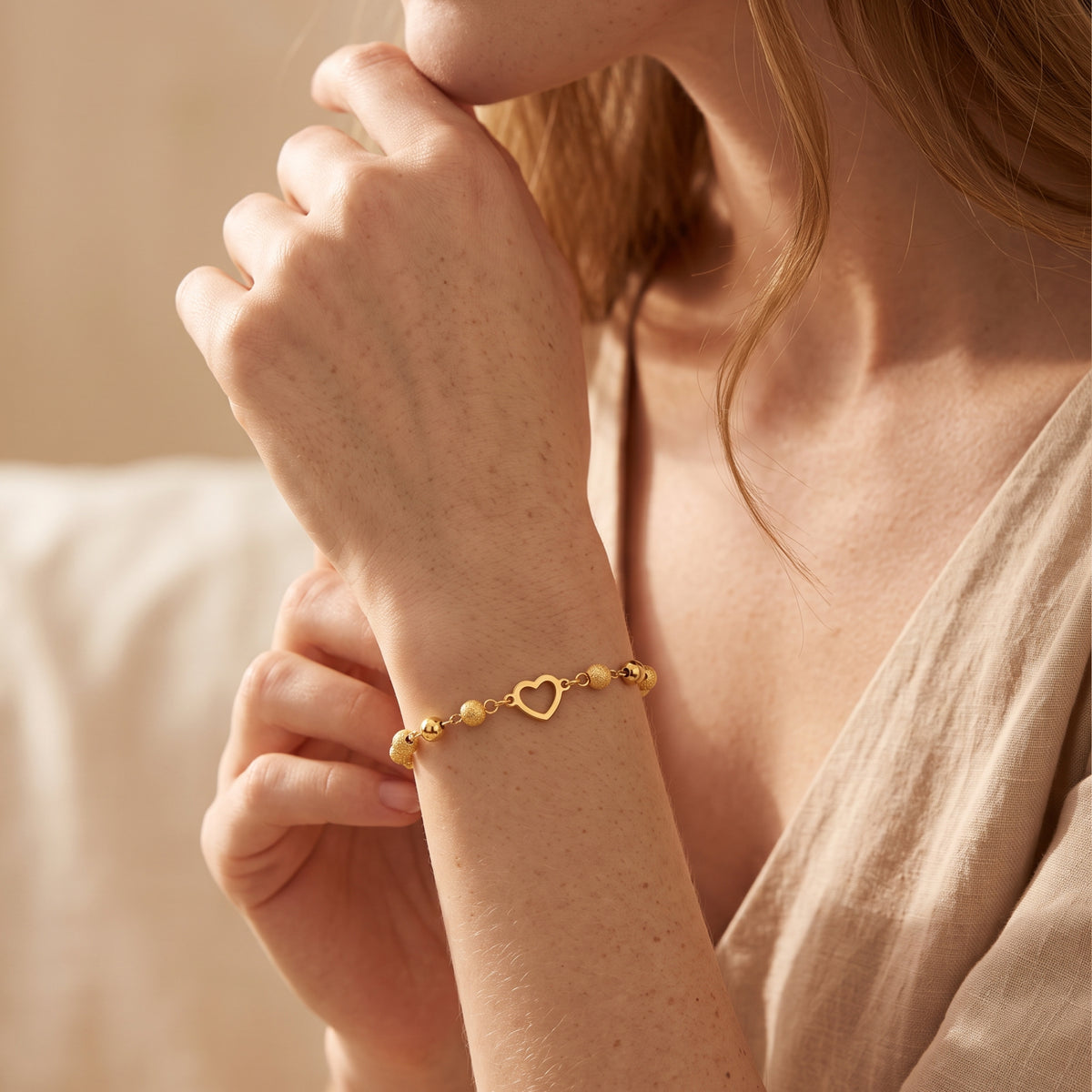 Model wearing the gold-tone heart station bracelet on her wrist with both hands raised near her chin.