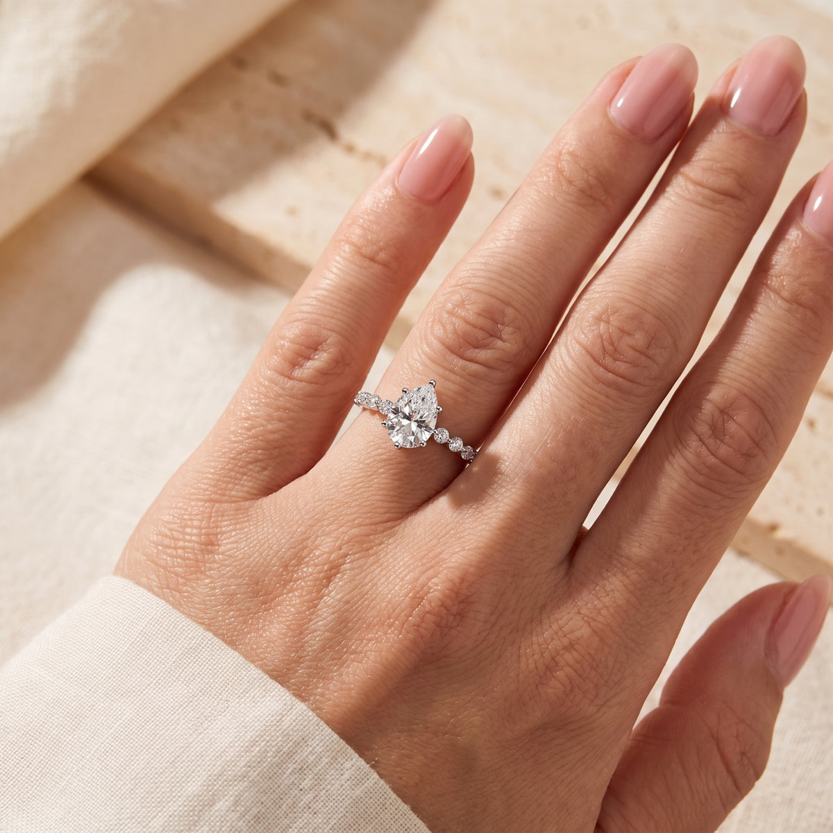 Silver ring with a pear-cut center stone worn on a hand, viewed straight-on against a neutral background.