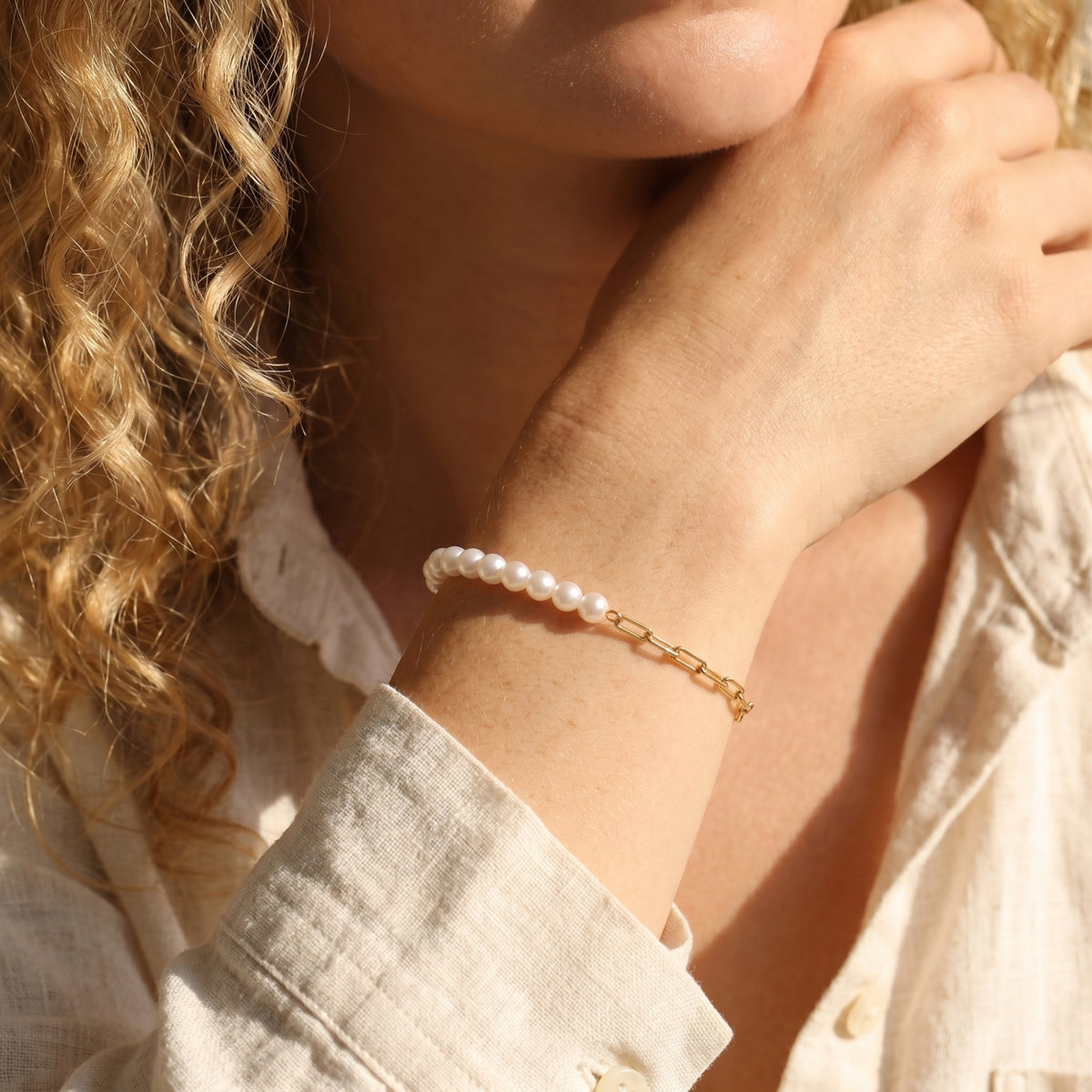 Woman wearing the solid gold and pearl Lenora bracelet on her wrist.