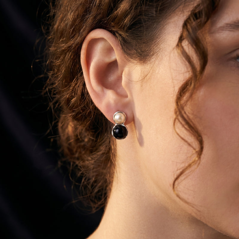 Woman wearing a silver drop earring featuring a round white pearl and black onyx cabochon.