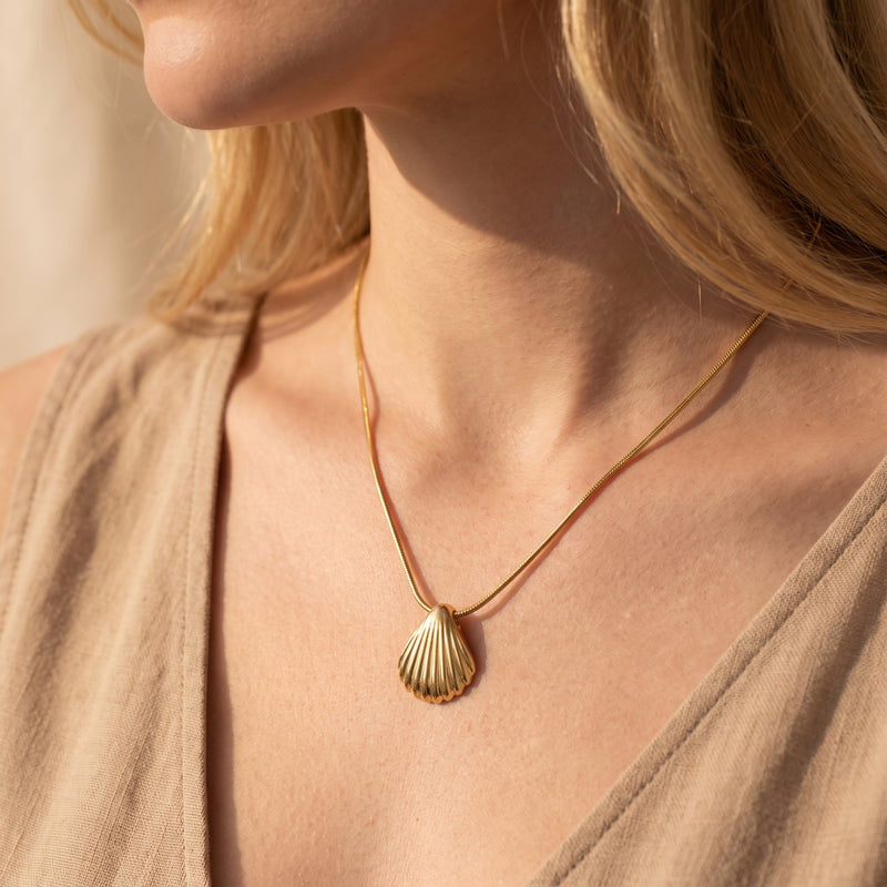 Model wearing the gold scallop shell pendant necklace with a sleeveless beige top.
