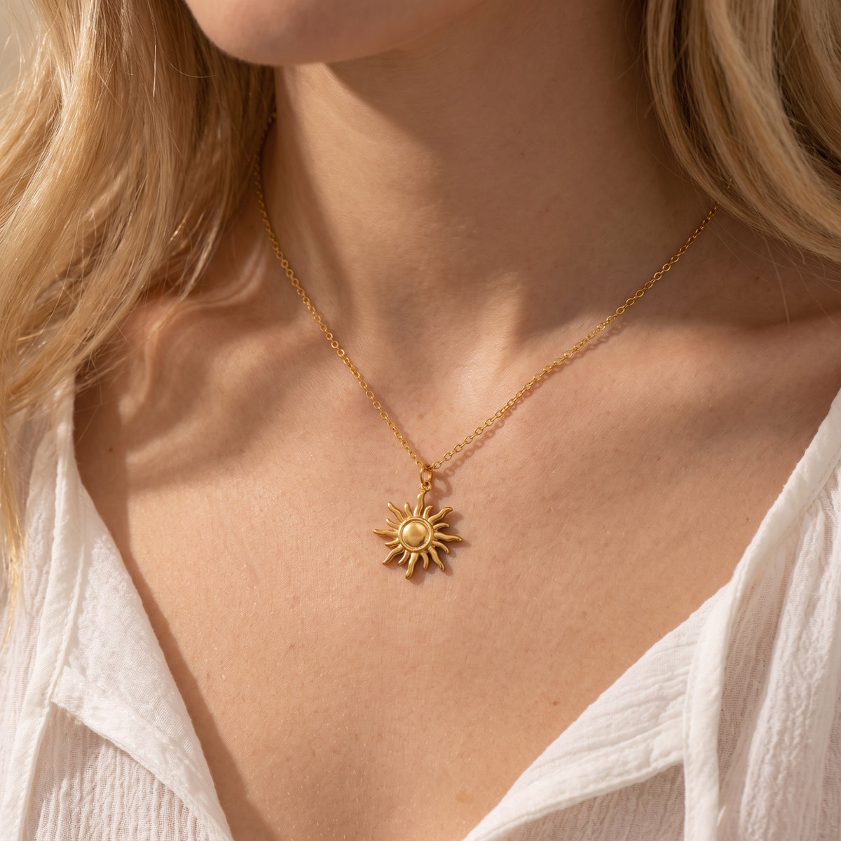 Close-up of a model wearing the gold sunburst pendant necklace with a delicate chain and white top.
