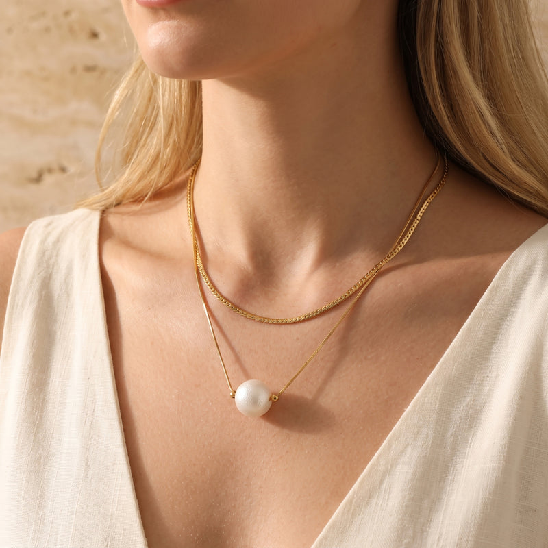 Close-up of a model wearing the gold-tone layered necklace with a white pearl pendant on her chest.