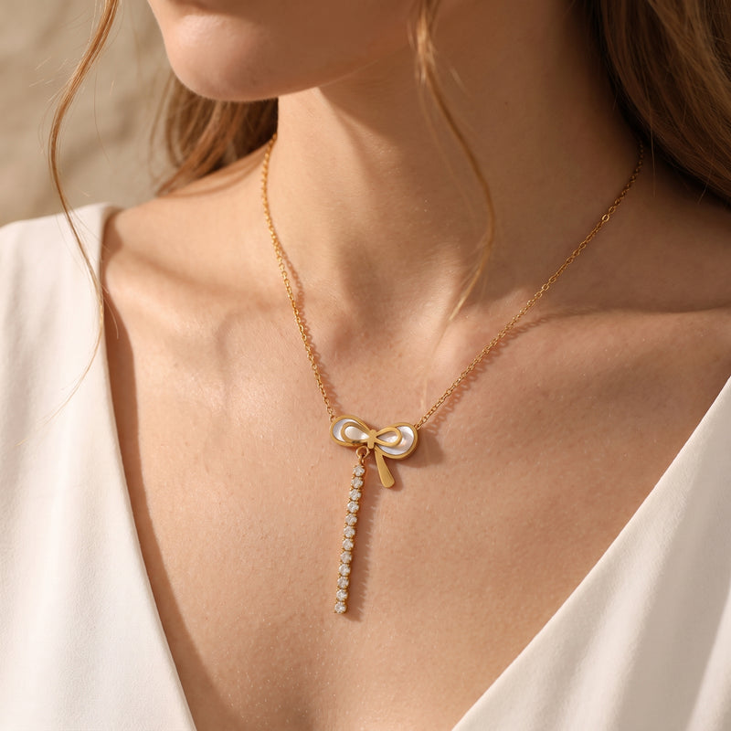 Model wearing the gold-tone bow necklace with pearlescent bow pendant and cascading clear stones over a white V-neck top.