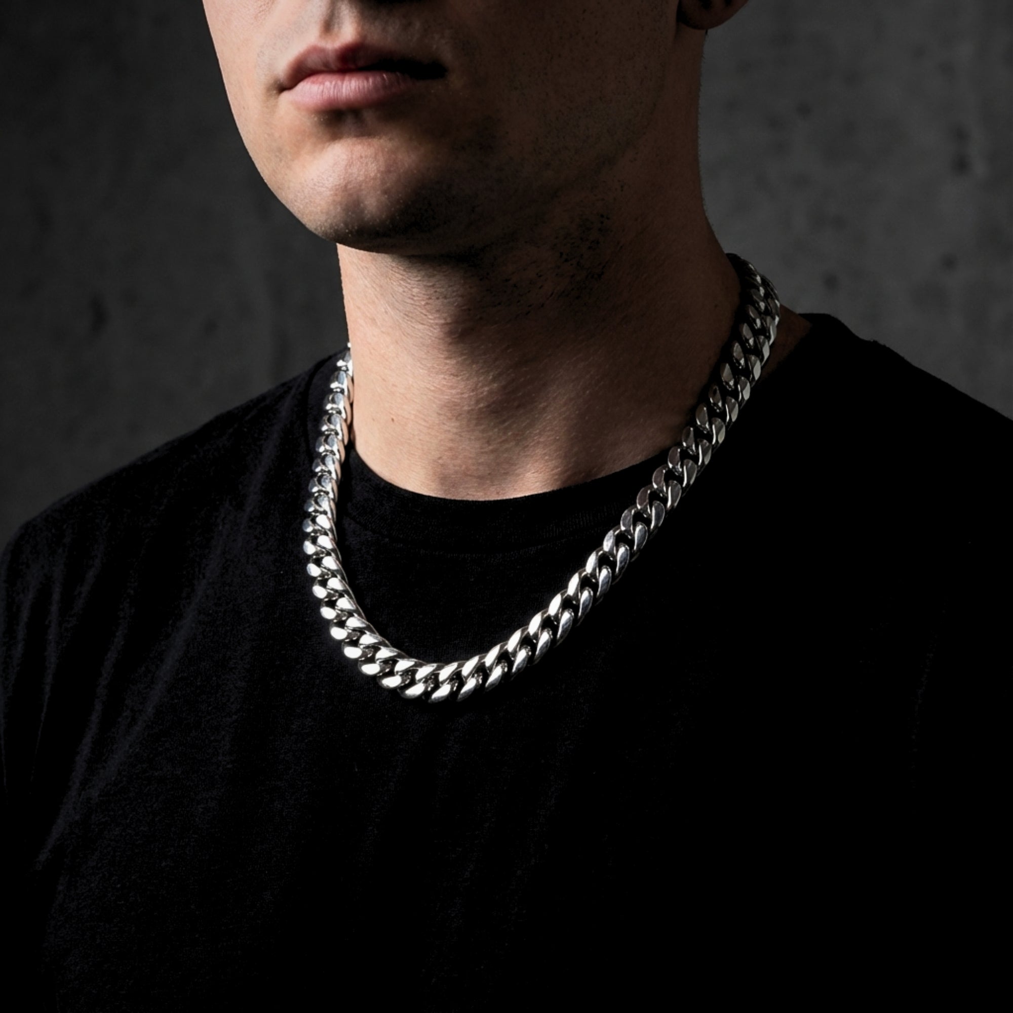 Man wearing a 12mm silver stainless steel Cuban link chain necklace over a black t-shirt.