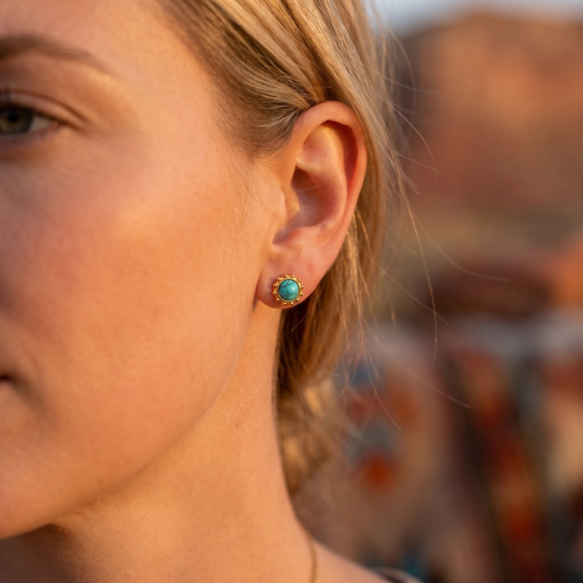 Model wearing a gold turquoise cabochon stud earring with a dotted bezel against a desert backdrop.