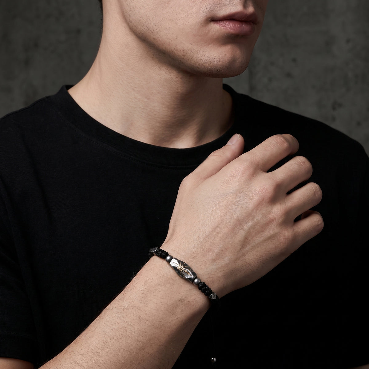 Sunburst rope bracelet worn on a wrist over a black shirt, with its carved focal station and braided black cord visible.