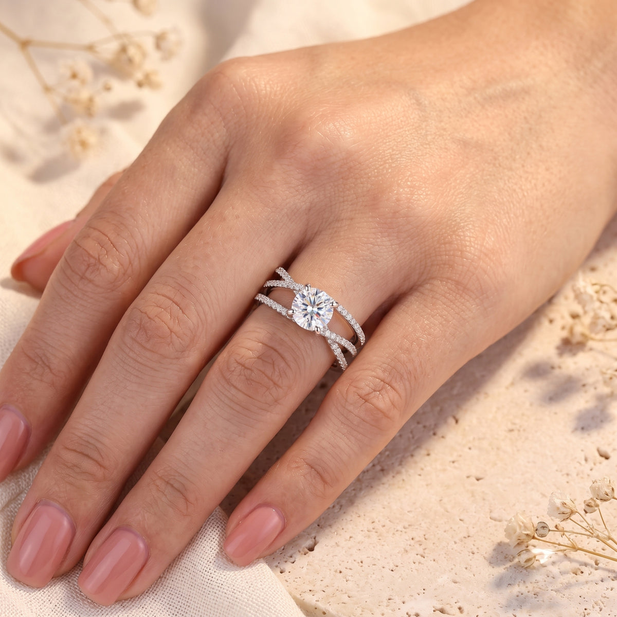 Silver criss-cross solitaire ring with round cut stone worn on a woman's hand.