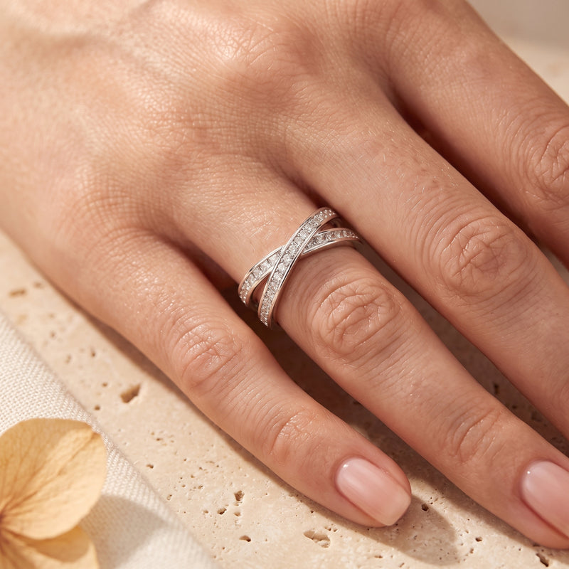 Silver crossover infinity ring with round simulated diamonds worn on a woman's hand.