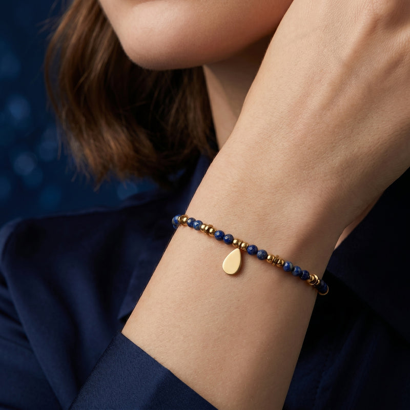 18K gold plated faceted 3mm lapis bead bracelet with a teardrop charm worn on a woman's wrist.