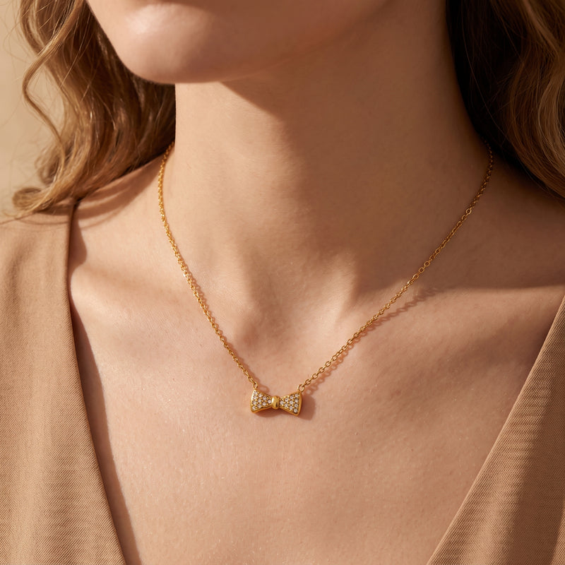 Model wearing the gold-tone bow pendant necklace with clear pave stones along the collarbone.