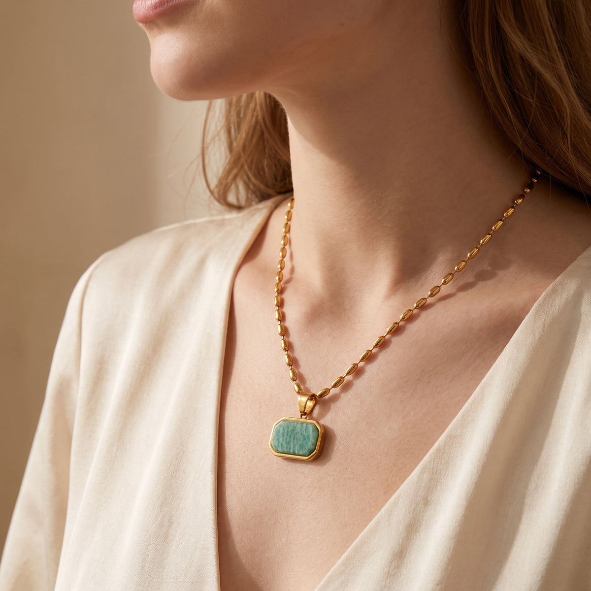 Model wearing a gold-tone bead chain necklace with an octagonal green Amazonite pendant over a V-neck top.