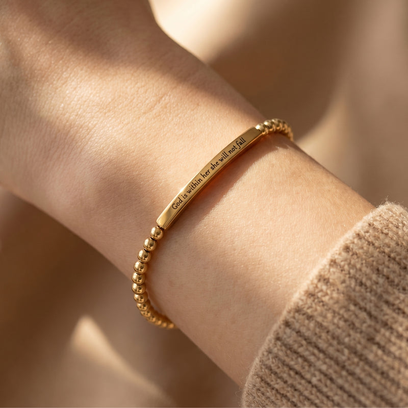 Gold engraved bar bracelet with beaded chain worn on a woman's wrist.