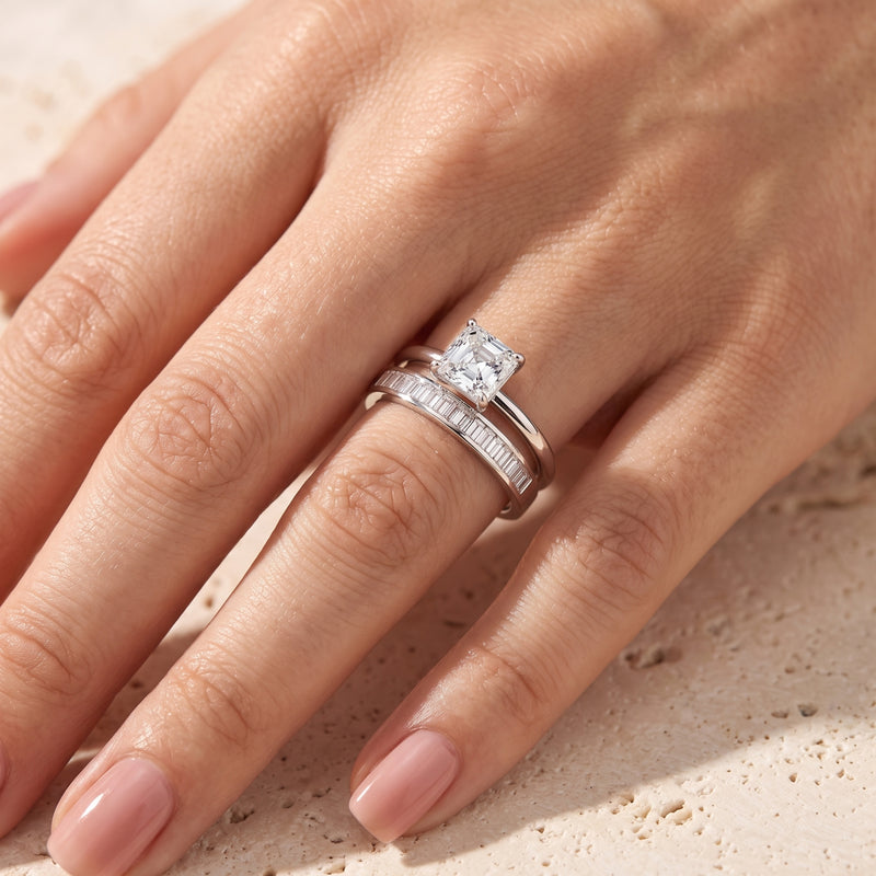 Square-cut simulated diamond solitaire and baguette eternity band in silver worn on a woman's ring finger.