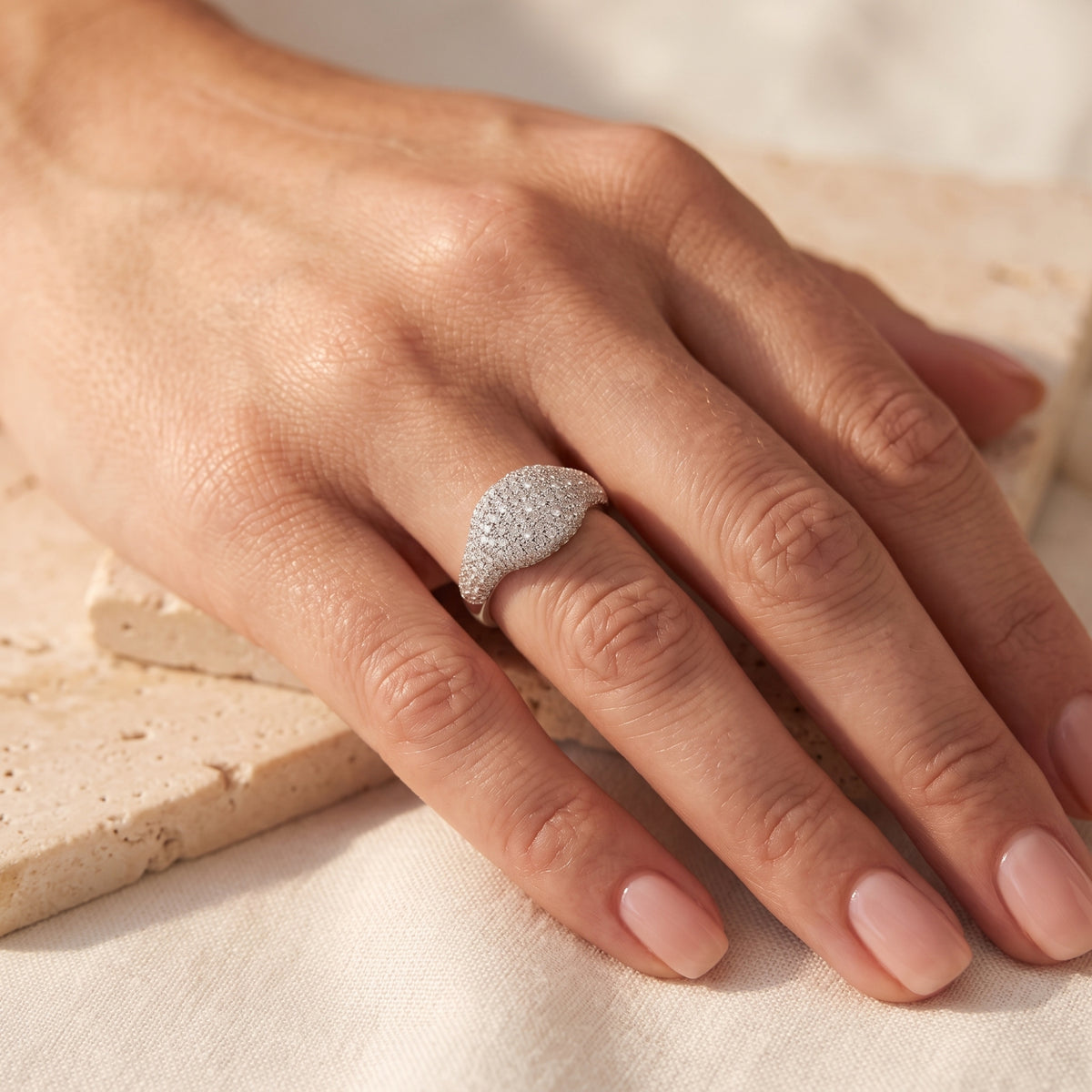Overhead view of a solid gold pave dome ring in white gold with clear simulated diamonds worn on a ring finger.