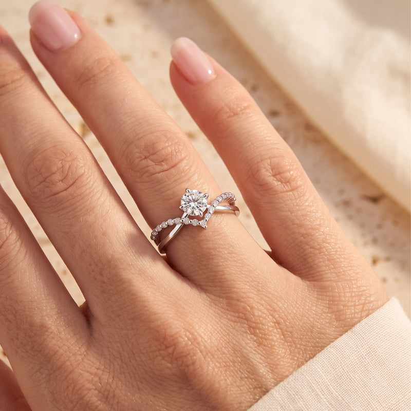 Silver criss-cross chevron split band ring with a round center stone worn on a finger.