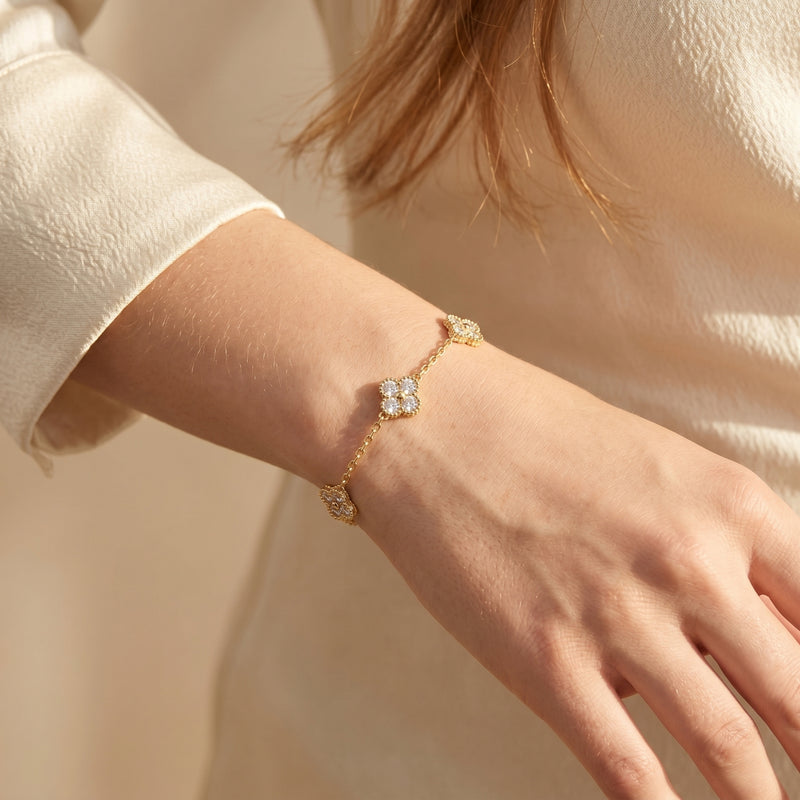Gold moissanite clover bracelet worn on a woman's wrist against a soft cream background.