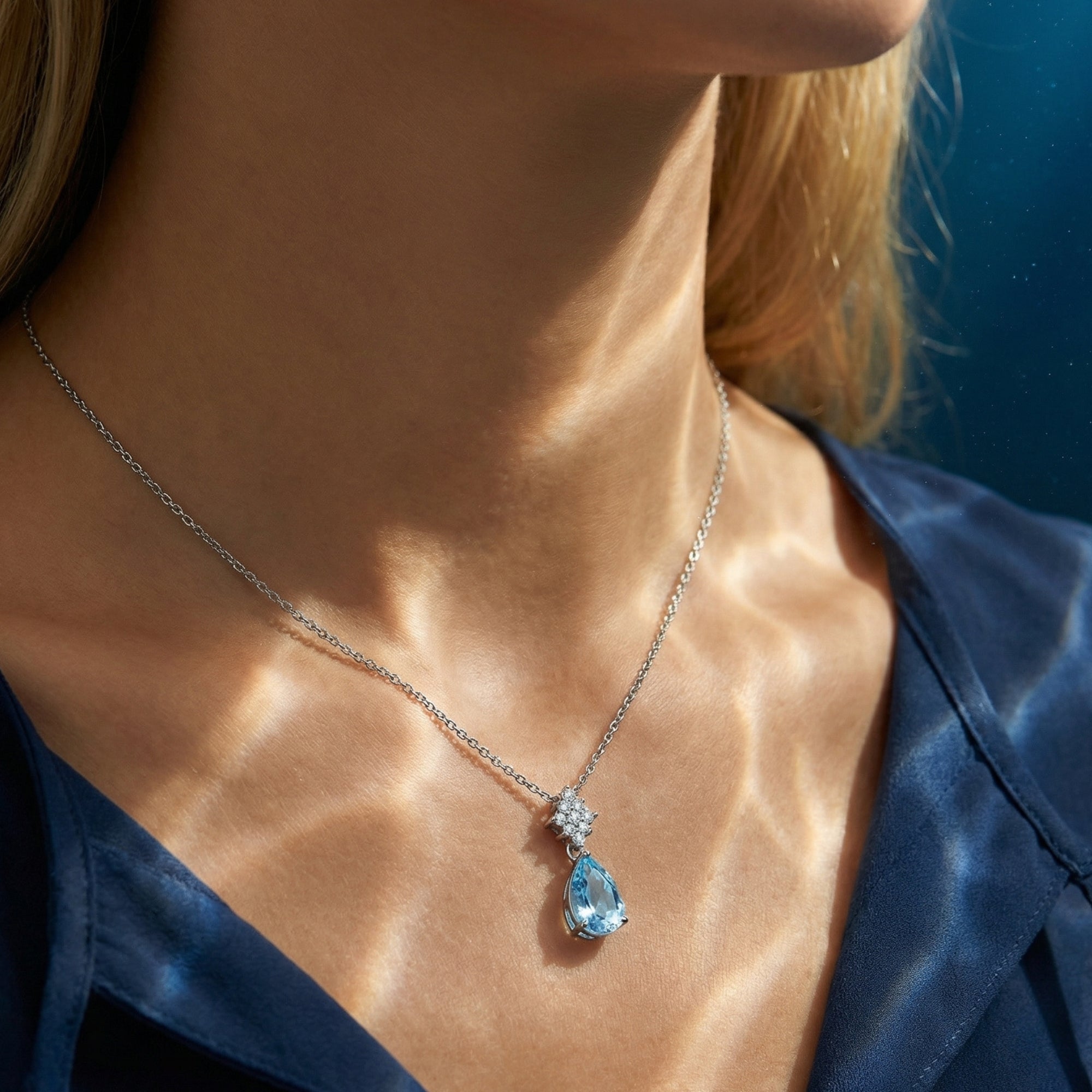 Model wearing the Oceania pear cut aquamarine necklace in platinum, showcasing the pendant against a blue shirt.