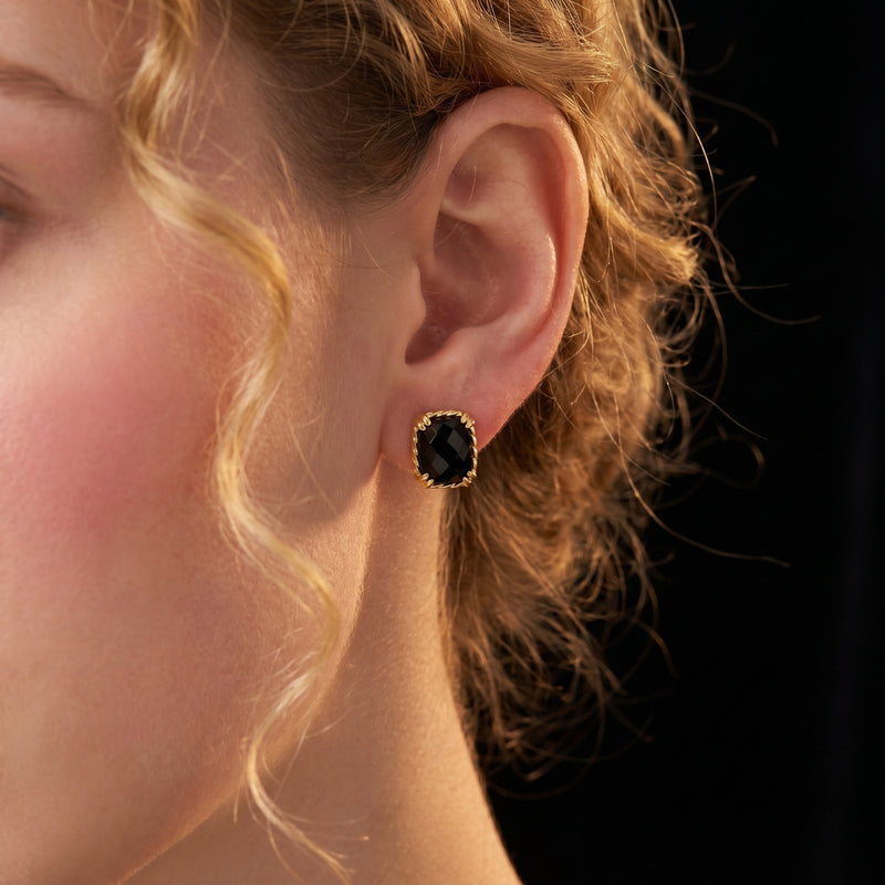 A woman wearing a gold square-cut faceted black onyx stud earring, showing the jewelry on the ear.