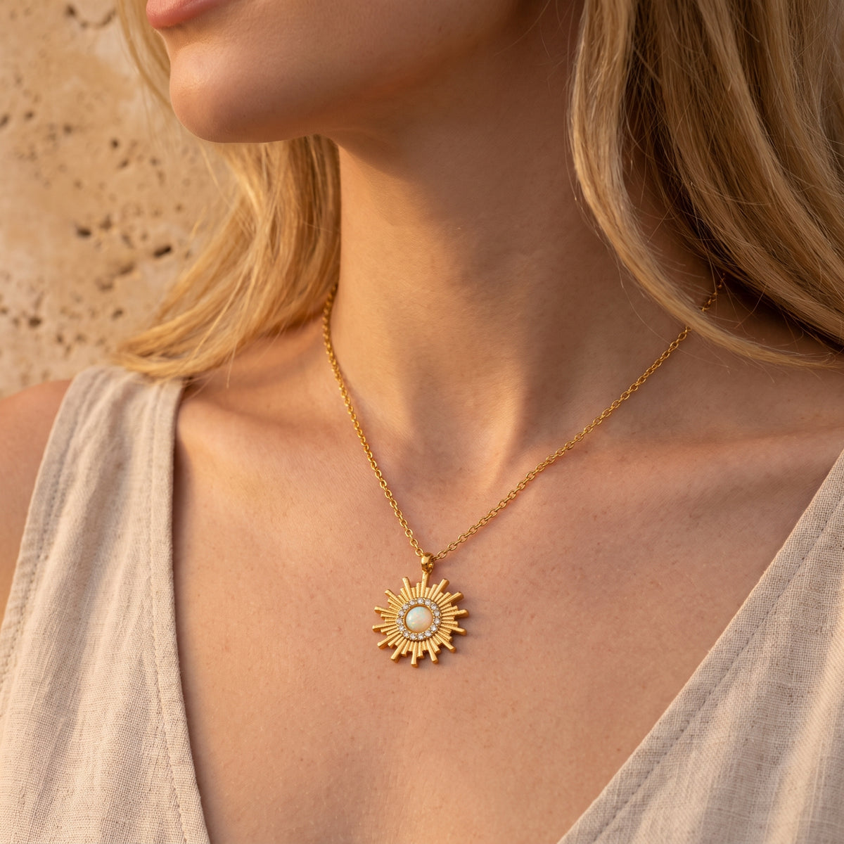 Close-up of a model wearing the gold-tone sunburst opal pendant necklace against a light beige top.