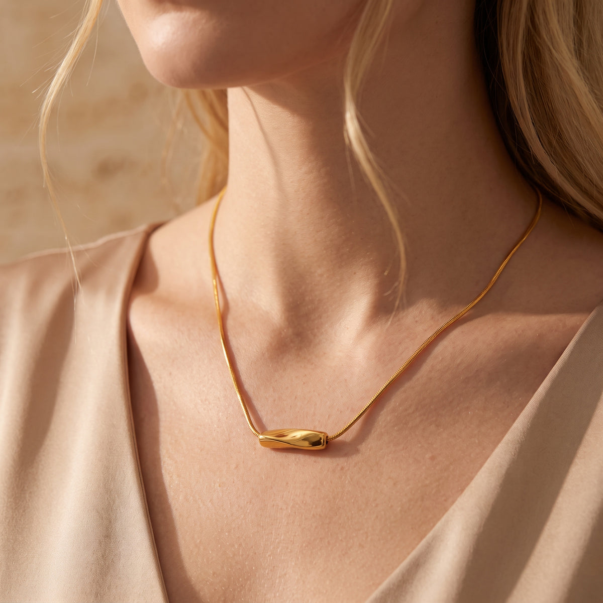 Close-up of a model wearing the gold-tone wave slide necklace over a beige top.