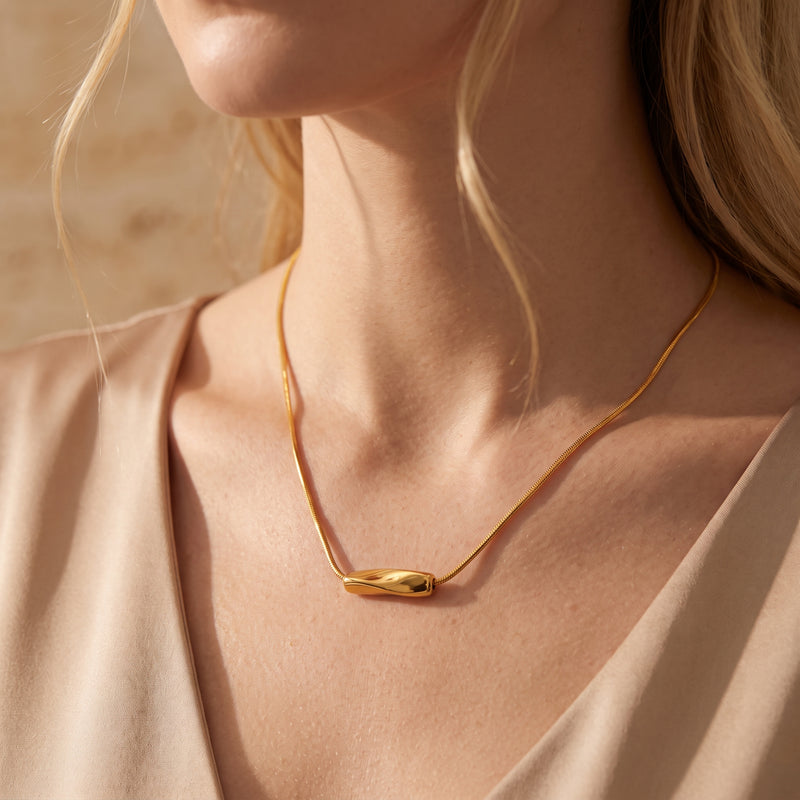 Close-up of a model wearing the gold-tone wave slide necklace over a beige top.
