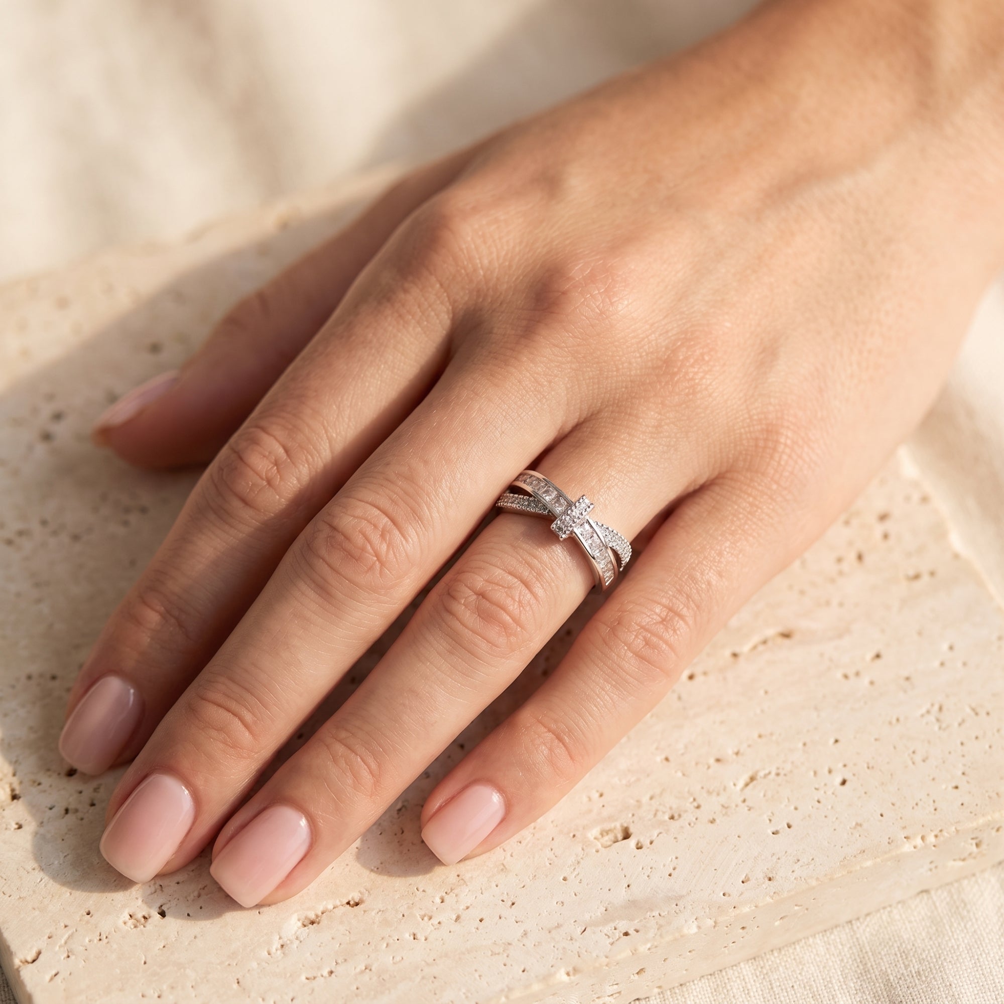 Top view of the Charlotte silver criss-cross ribbon ring with simulated diamonds worn on a woman's hand.