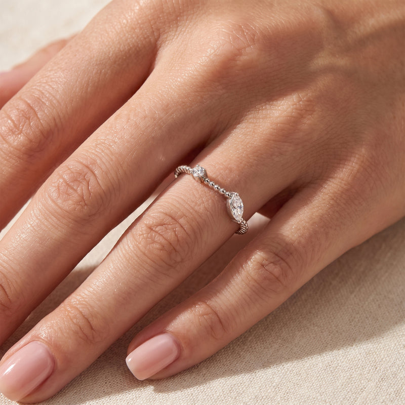 Close-up of the silver beaded bypass ring with clear marquise and round stones worn on a finger.