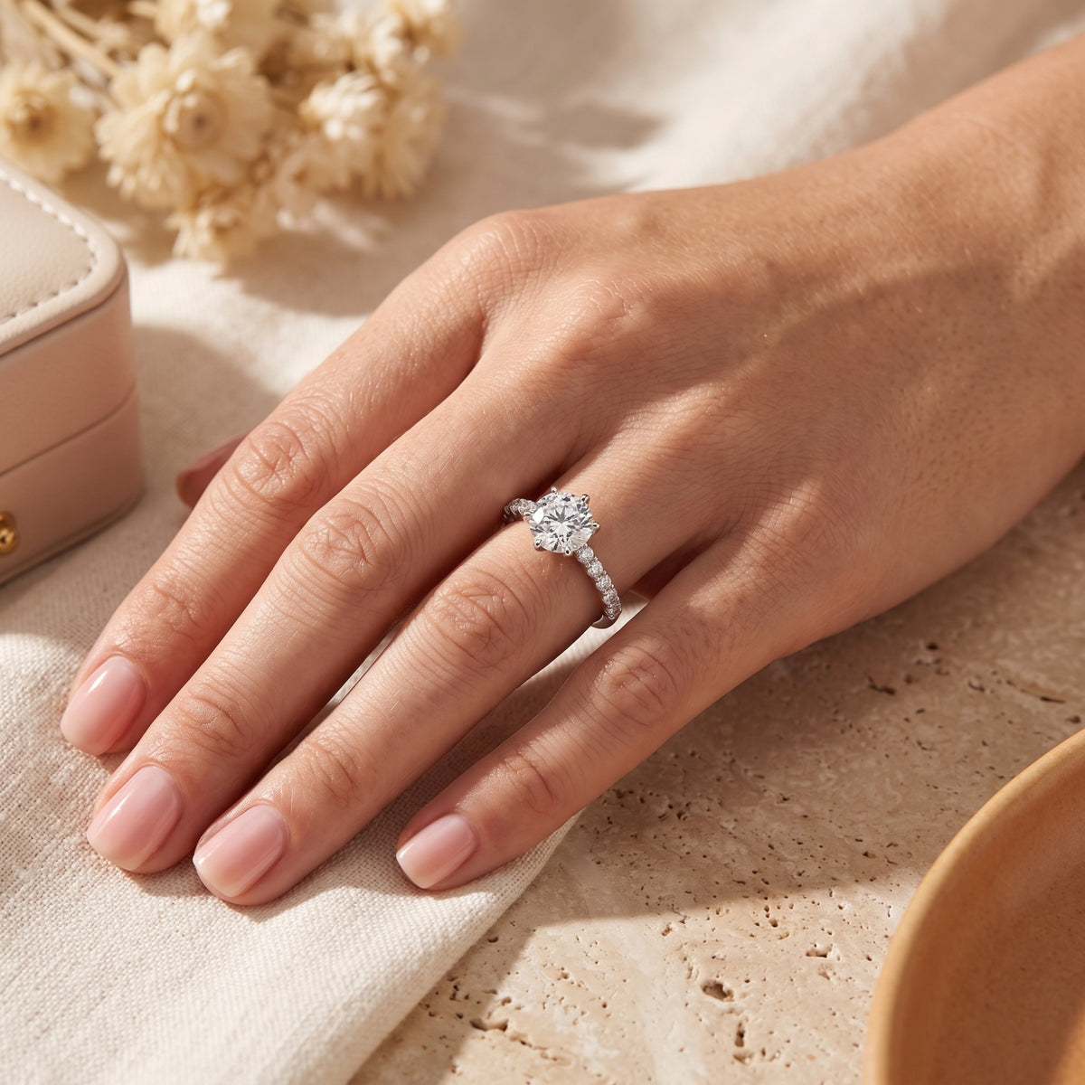 Silver solitaire ring with a round clear center stone and pavé band worn on a hand against a cream background.