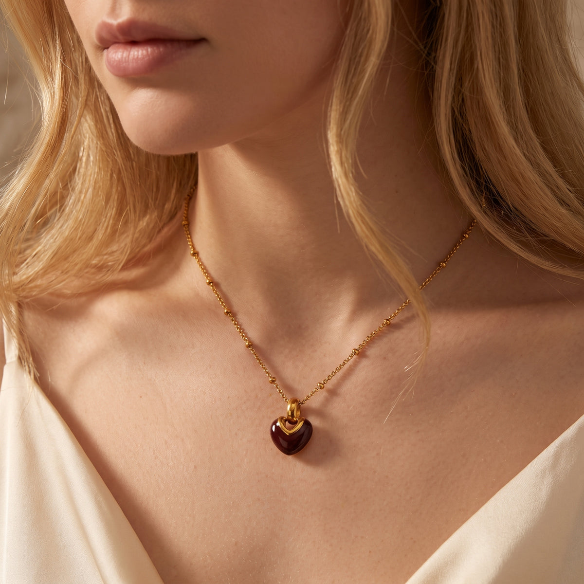 Close-up view of a woman wearing the gold-tone beaded necklace with a glossy crimson heart pendant.