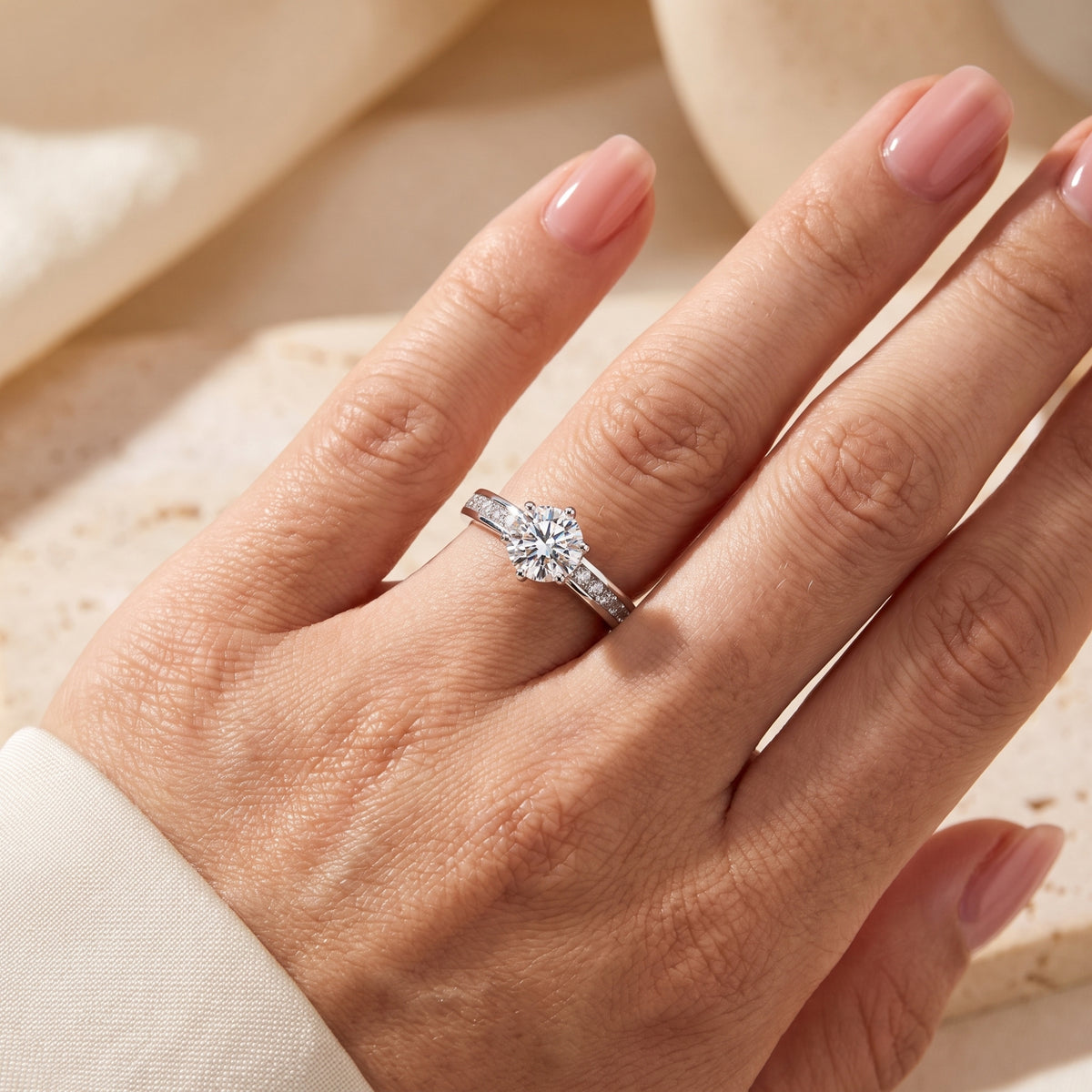 Close-up of the silver round solitaire ring worn on a hand against a soft warm backdrop.