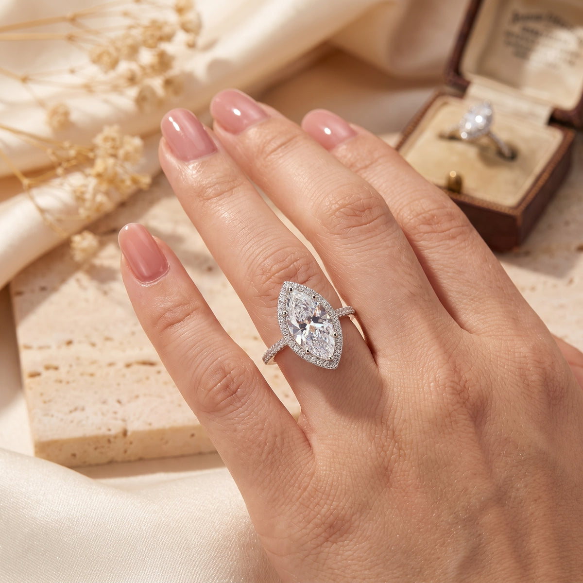 Hand wearing a silver marquise halo ring beside an open jewelry box.