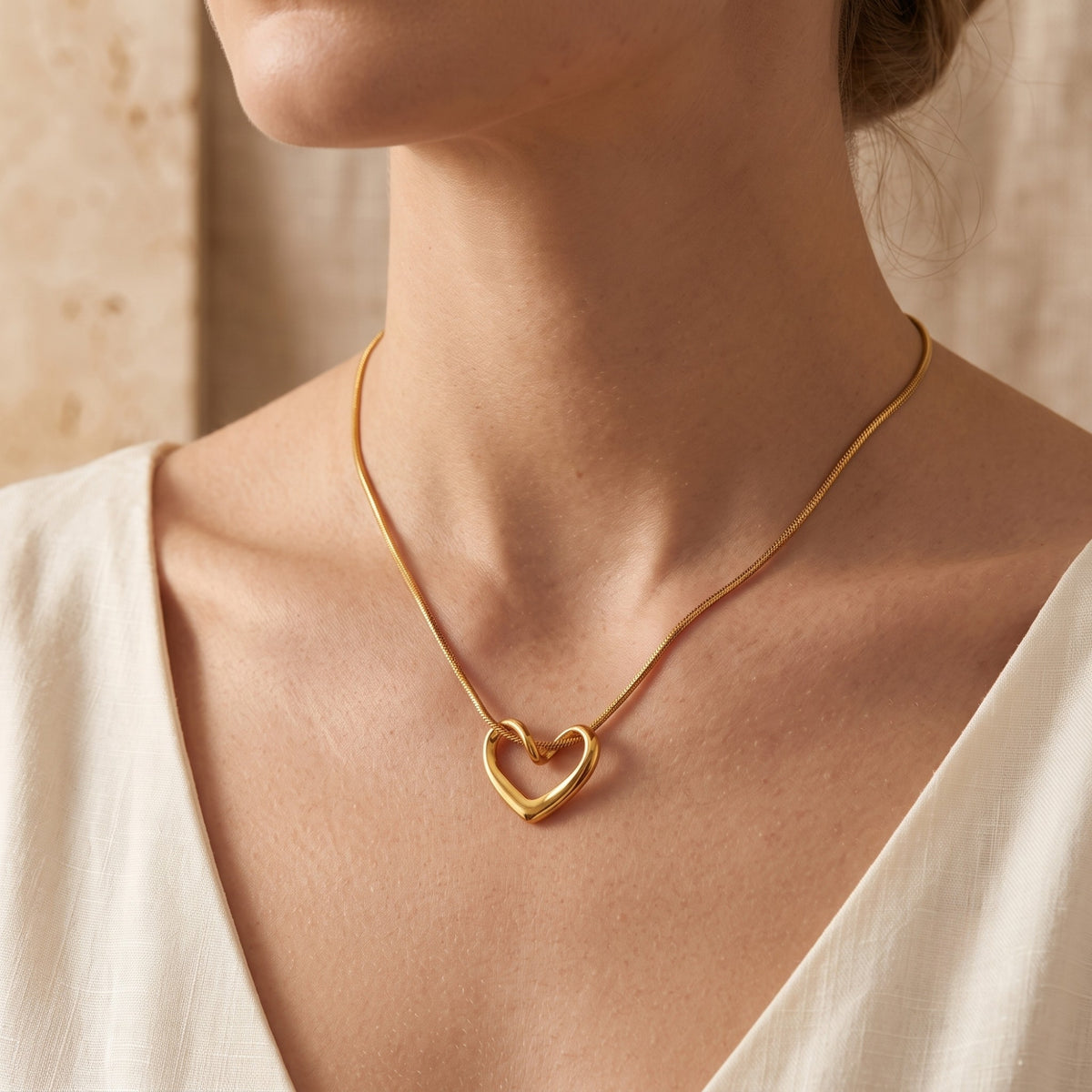 Model wearing the gold-tone fluid open heart necklace on a snake chain with a white V-neck top.