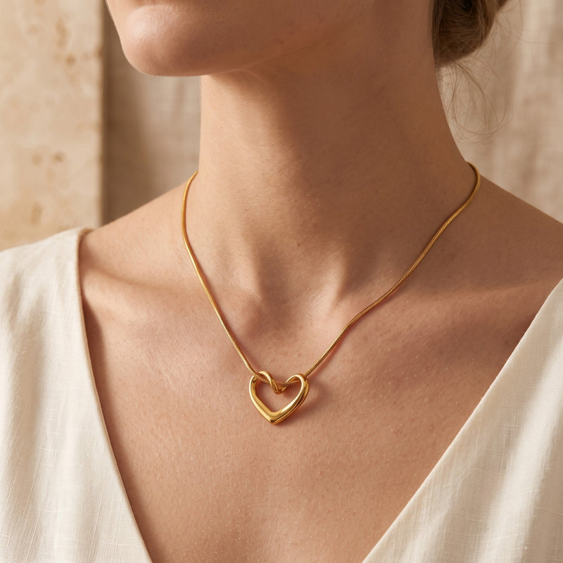 Model wearing the gold-tone fluid open heart necklace on a snake chain with a white V-neck top.