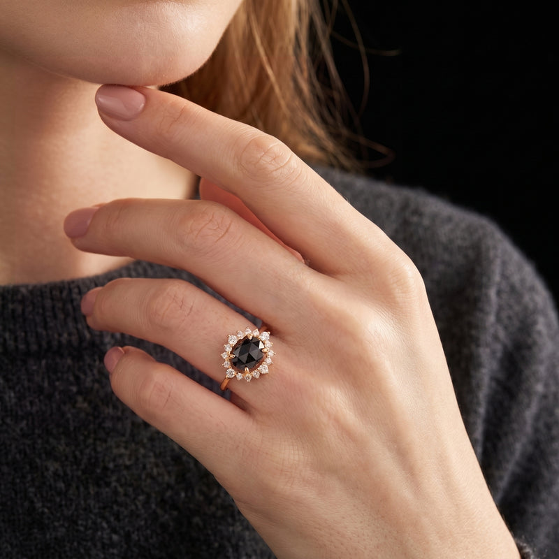 The 18K gold plated Aurelius ring with an oval black onyx and halo, worn on a model's hand near her face.